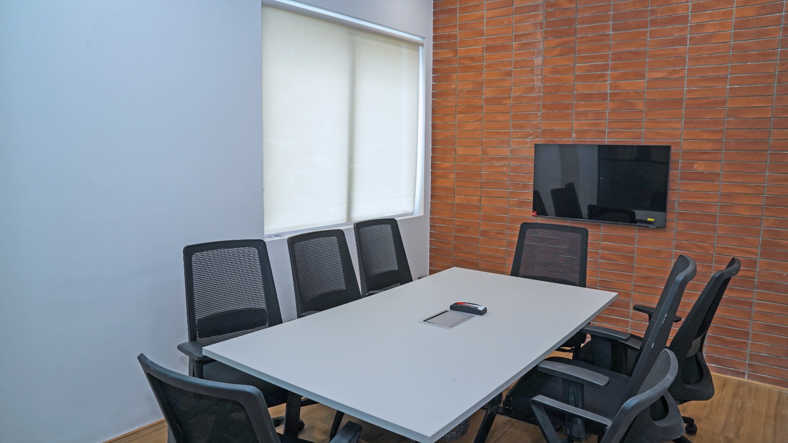 Discussion room with a six-seat meeting table and wall-mounted screen in the plug and play office space at Capstone House Bangalore
